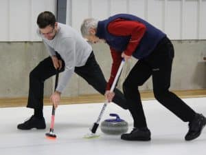 Photo of two curlers sweeping ahead of the stone during play at the Norfolk, Connecticut, Curl9ng Club.